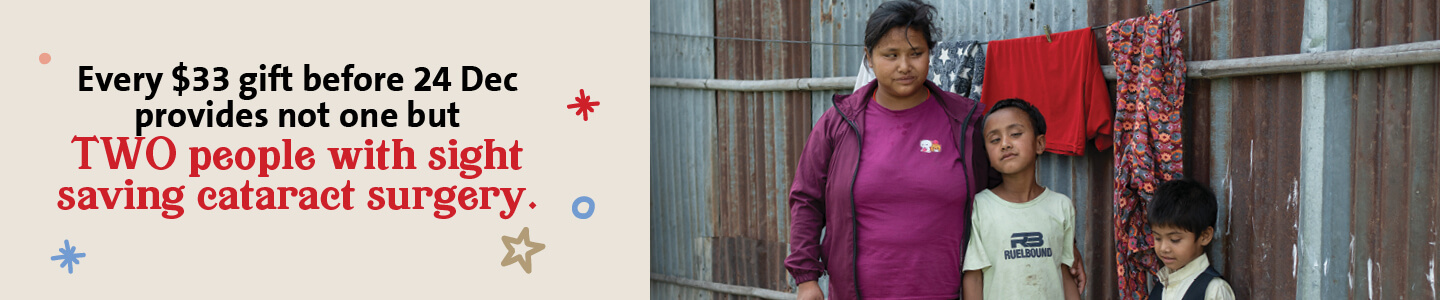 A woman in a purple top stands with three children in front of a corrugated metal wall, with colorful clothes hanging behind them. Text below reads: 'Every $33 gift before 24 Dec provides not one but TWO people with sight saving cataract surgery'